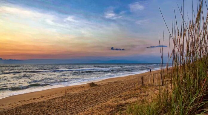 Alba colorata su una spiaggia della Carolina del Nord, onde che si infrangono su una spiaggia sabbiosa incorniciata da dune d'erba.  Anatra, Carolina del Nord