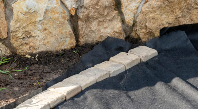 Bordatura di tessuto geotessile posato con pavimentazioni in arenaria nel giardino estivo in fase di ricostruzione