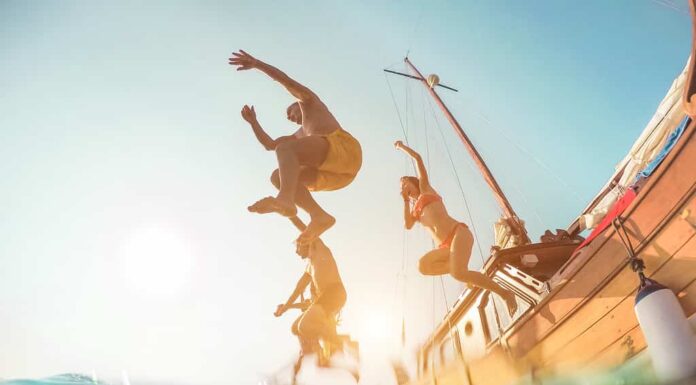 Amici felici che si tuffano in mare dalla barca a vela - Giovani che saltano nell'oceano durante un'escursione estiva - Concetto di vacanza, gioventù e divertimento - Focus principale sull'uomo in primo piano - Distorsione della lente fisheye