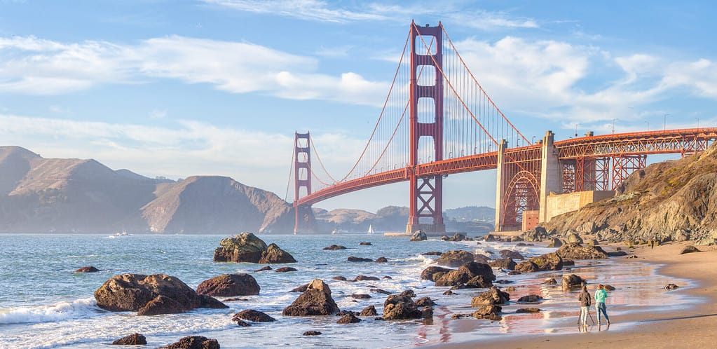 Classica vista panoramica del famoso Golden Gate Bridge visto dalla pittoresca Baker Beach nella splendida luce dorata della sera in una giornata soleggiata con cielo azzurro e nuvole in estate, San Francisco, California, Stati Uniti