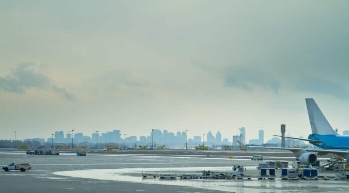 L'asfalto di un aeroporto, che mostra la parte posteriore di un aereo passeggeri e i veicoli di servizio che lo circondano, con lo skyline di una città dietro.  Aeroporto Internazionale Pearson di Toronto, Ontario.