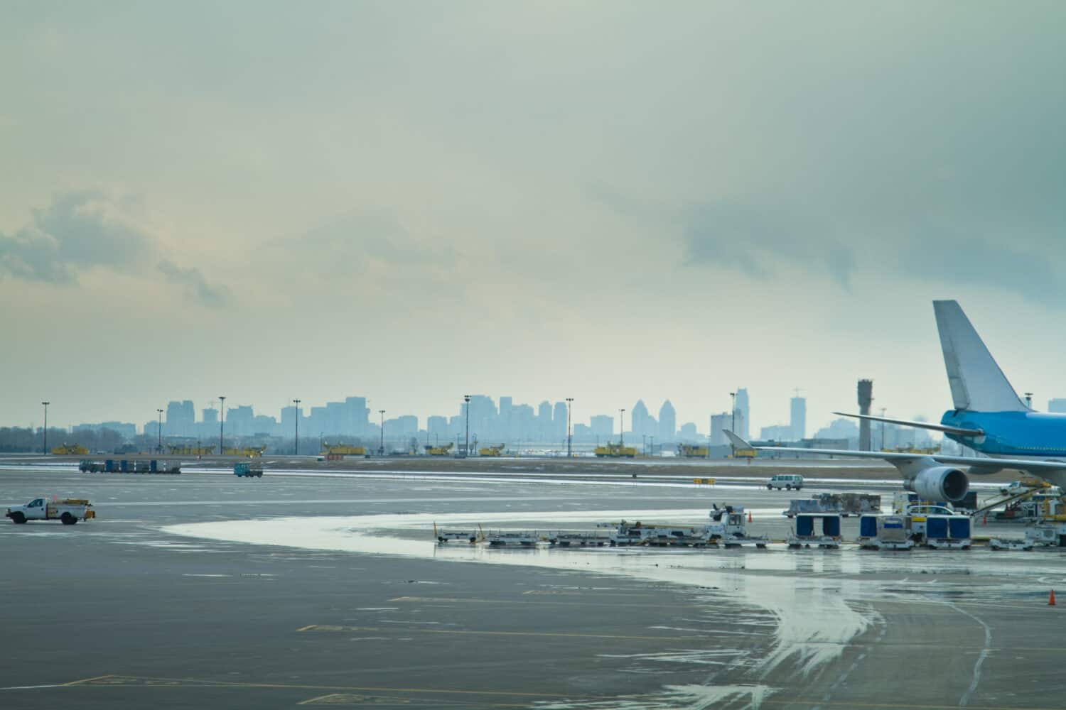 L'asfalto di un aeroporto, che mostra la parte posteriore di un aereo passeggeri e i veicoli di servizio che lo circondano, con lo skyline di una città dietro.  Aeroporto Internazionale Pearson di Toronto, Ontario.