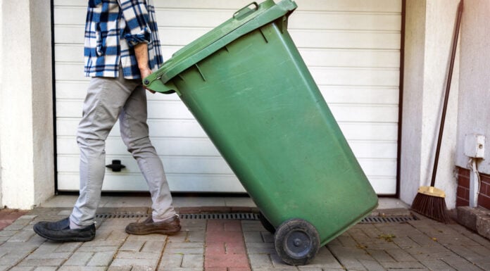 Uomo anziano che rotola il bidone della spazzatura