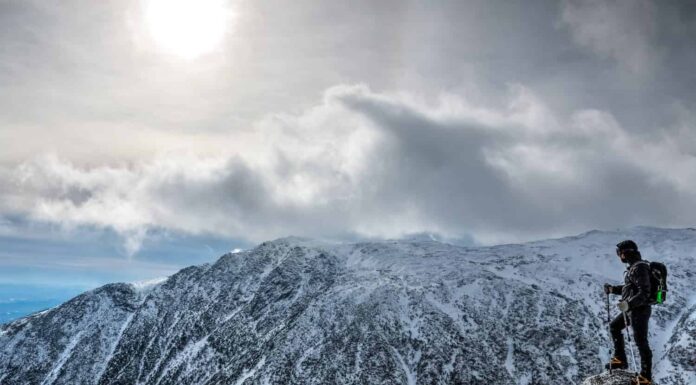 Uomo con l'attrezzatura al limite, che fa un'escursione sul monte Washington in inverno, guardando oltre il burrone.  New Hampshire, Stati Uniti
