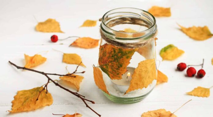 Candela fai da te a tema autunnale.  Candela tealight in barattolo di vetro, decorata con foglie dorate essiccate.  Arredamento d'interni in autunno. 