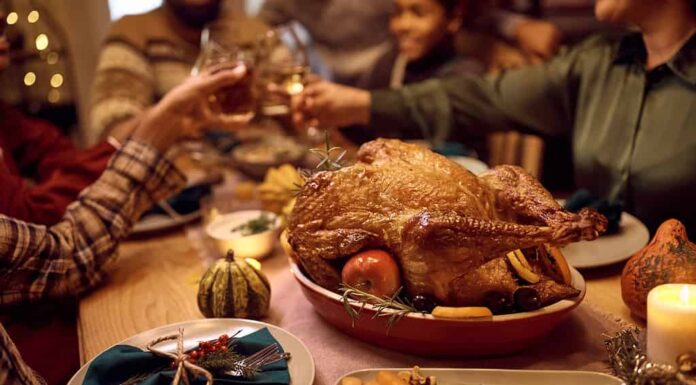 Primo piano di tacchino ripieno durante il pasto del Ringraziamento con brindisi in famiglia sullo sfondo.