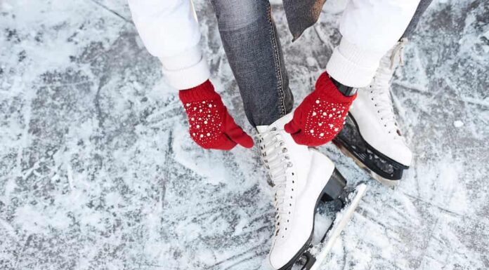 Ragazza che allaccia i lacci delle scarpe sui pattini da ghiaccio prima di pattinare sulla pista di pattinaggio, mani con guanti a maglia rossi.
