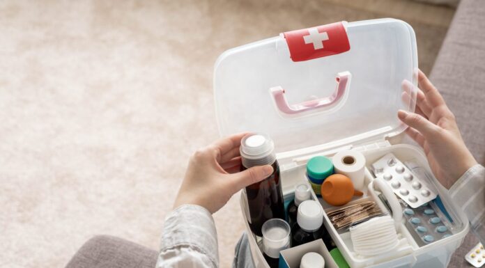 Primo piano della mano femminile che posiziona ordinatamente il medicinale nella vista dall'alto del kit di pronto soccorso domestico.  Organizzazione di stoccaggio in scatola di plastica trasparente per farmaci, pillole, siringhe, bende.  Fornitura rapida di emergenza per la sicurezza dell'aiuto sanitario