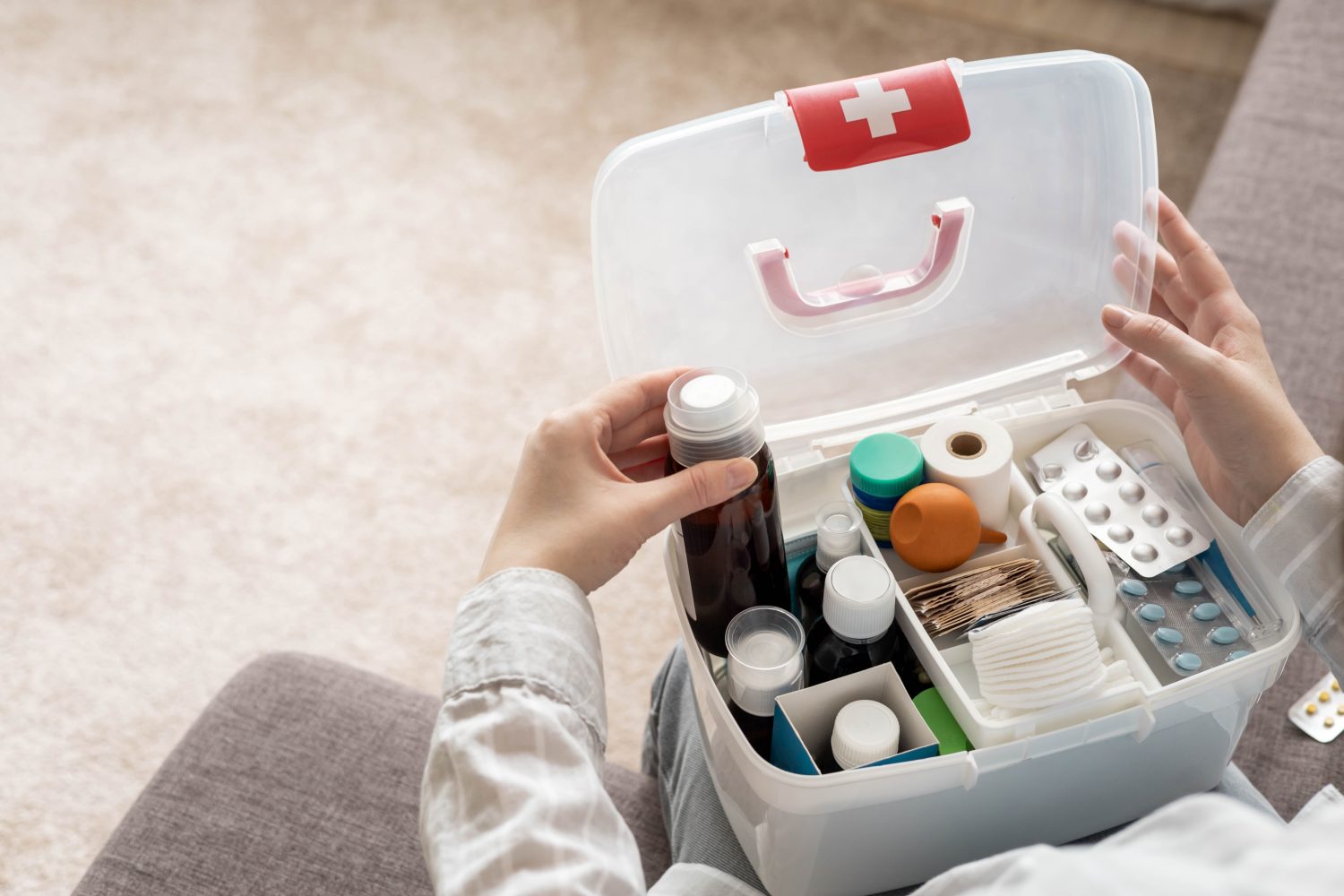 Primo piano della mano femminile che posiziona ordinatamente il medicinale nella vista dall'alto del kit di pronto soccorso domestico.  Organizzazione di stoccaggio in scatola di plastica trasparente per farmaci, pillole, siringhe, bende.  Fornitura rapida di emergenza per la sicurezza dell'aiuto sanitario