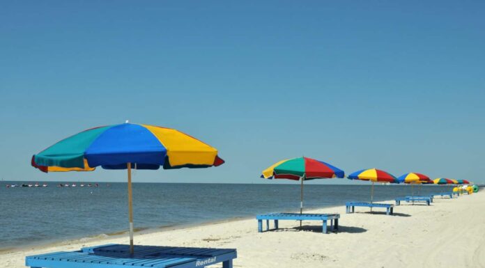 Sedie a sdraio, ombrelloni e trike di grandi dimensioni sparsi lungo la spiaggia di Biloxi nel Mississippi in una giornata primaverile.