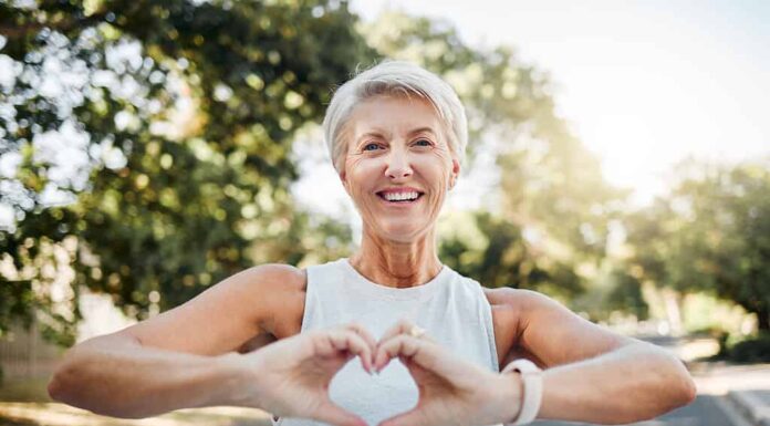 Mani fitness, felici e cardiache di un'anziana nella natura dopo aver corso per salute, benessere e allenamento.  Sorridi, motivazione e pace con la signora anziana e segno di amore, fede e formazione nella natura