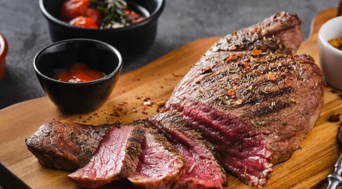 Succosa bistecca di manzo di marmo mediamente cotta con salsa su tavola di legno, primo piano.  Messa a fuoco selettiva.