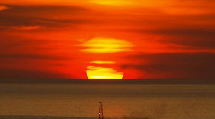 Grande tramonto rotondo nascosto dietro le nuvole sopra l'orizzonte sul Golfo del Messico (dal Messico Campache) con la sagoma di una grande nave