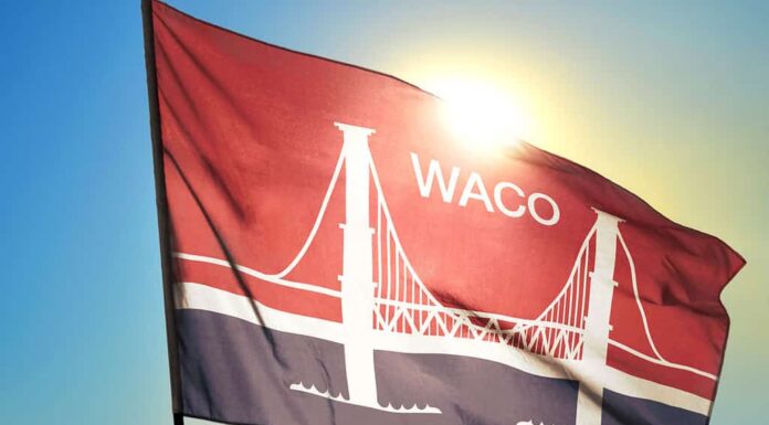 Bandiera di Waco del Texas degli Stati Uniti che sventola nel vento davanti al sole