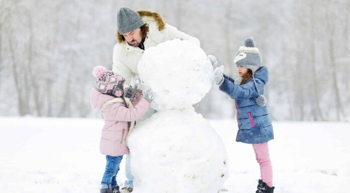 Giovane padre e le sue figlie che costruiscono un pupazzo di neve