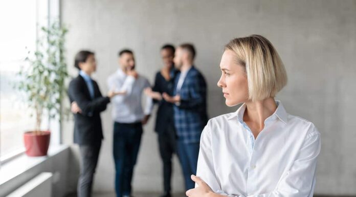 Colleghi maschi che sussurrano dietro la schiena di una donna d'affari infelice in ufficio