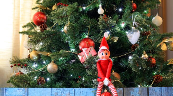 Elfo Dispettoso Sullo Scaffale Seduto Su Un Ramo Di Un Albero Di Natale Con Una Pallina.