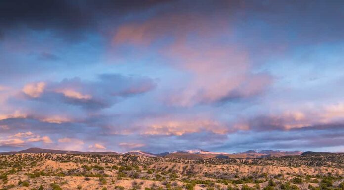 Nuvole colorate drammatiche su un paesaggio desertico e montano al tramonto