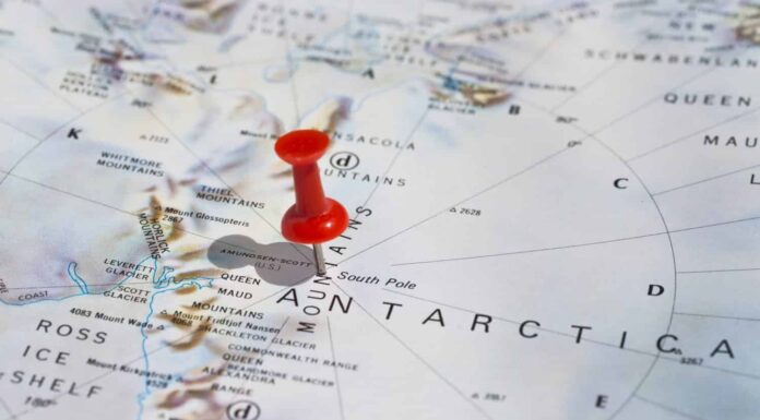 Polo Sud segnato sulla mappa con puntina rossa.  Messa a fuoco selettiva sulla parola Polo Sud e sulla puntina da disegno.  Il perno è in un angolo e proietta un'ombra a sinistra. 