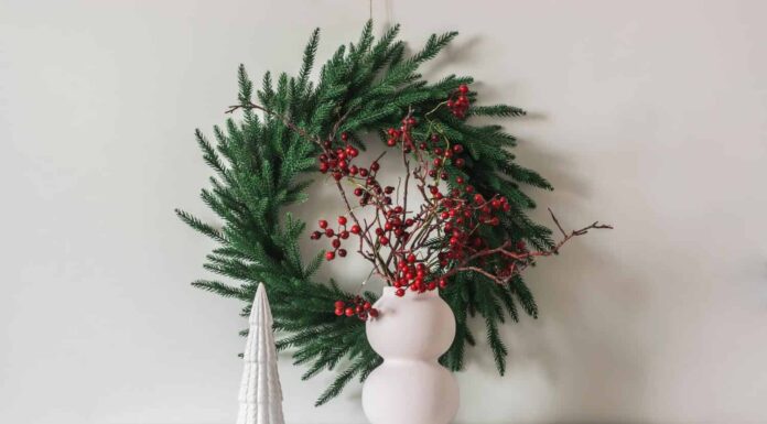 Decorazioni natalizie in stile scandinavo nel soggiorno: una ghirlanda di abete rosso sul muro, un vaso con rami di mirtillo rosso su una cassettiera bianca