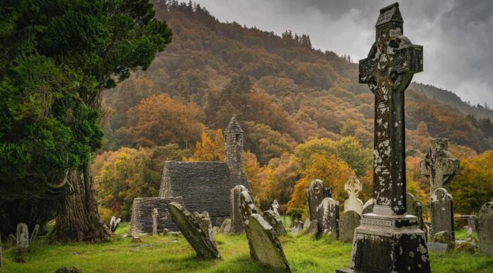 Tombe antiche della chiesa medievale Croci celtiche nel cimitero di Glendalough.  Foresta autunnale lunatica, montagne sotto la pioggia, cielo tempestoso sullo sfondo Wicklow Irlanda
