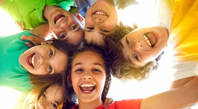Gruppo di bambini allegri, gioiosi e carini che giocano insieme e si divertono.  Ritratto di gruppo di bambini felici che si stringono, guardando la telecamera e sorridendo.  Angolo basso, vista dal basso.  Concetto di amicizia