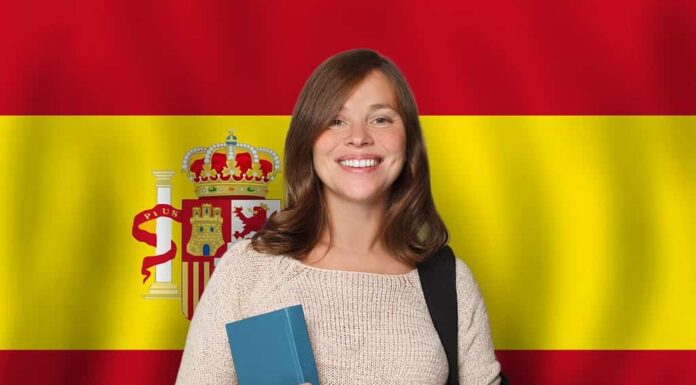 Studentessa allegra sullo sfondo della bandiera spagnola.  Viaggiare, studiare e imparare la lingua nel concetto di Spagna