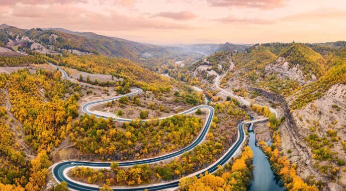 Vista panoramica aerea del fiume Venetikos e della strada tortuosa nella foresta autunnale nella Grecia balcanica.  Parco naturale e infrastrutture di trasporto