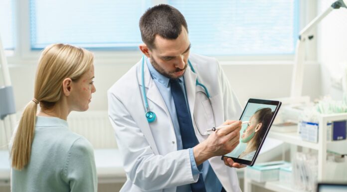 Il chirurgo plastico/estetico consulta una donna in merito all'intervento di lifting facciale, disegna frecce sullo schermo del computer del tablet digitale, mostrando i tipi di lifting facciale e procedure di correzione del naso disponibili per lei.