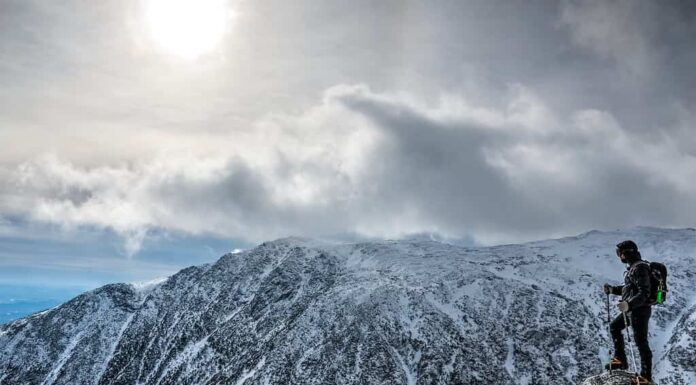 Uomo con l'attrezzatura al limite, che fa un'escursione sul monte Washington in inverno, guardando oltre il burrone.  New Hampshire, Stati Uniti