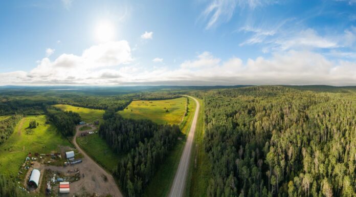 Vista panoramica sulla strada vicino al tramonto, circondata da foreste, terreni agricoli e industria.  Ripresa aerea del drone.  A nord-ovest di Fort Nelson, Alaska Highway, Columbia Britannica settentrionale.
