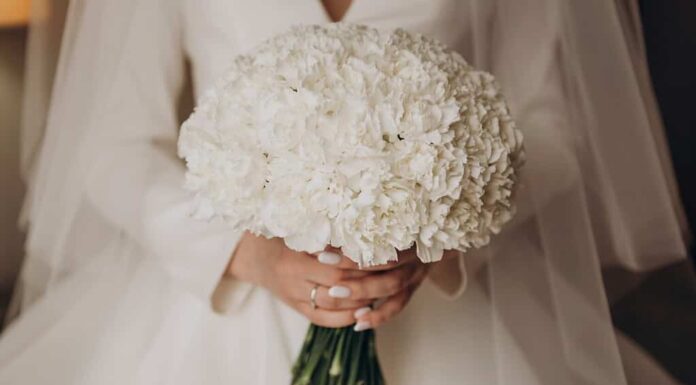 La sposa in abito da sposa bianco tiene in mano un mazzo di garofani bianchi.  Matrimonio, fidanzamento.  Sposa e sposo