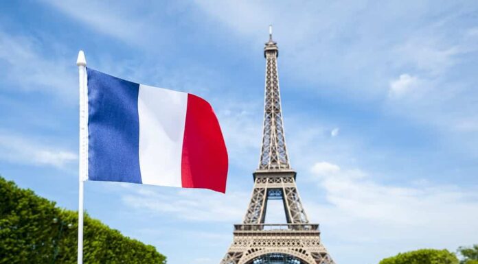 Bandiera francese che sventola nel cielo azzurro primaverile di fronte alla Torre Eiffel a Parigi, Francia