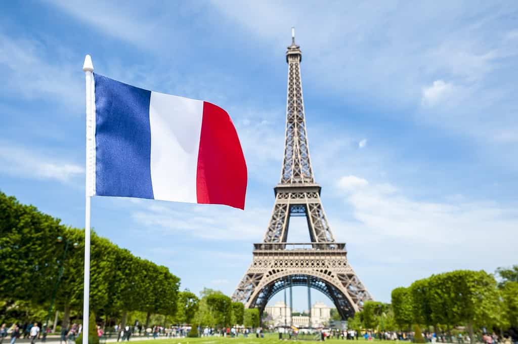 Bandiera francese che sventola nel cielo azzurro primaverile di fronte alla Torre Eiffel a Parigi, Francia