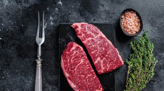 Bistecca fresca di Denver cruda Carne di manzo in marmo con erbe aromatiche.  Sfondo nero.  Vista dall'alto