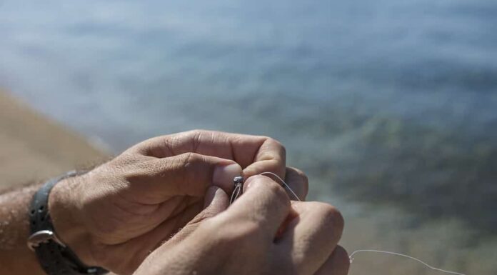 Un uomo annoda un amo da pesca e un piombo sulla spiaggia