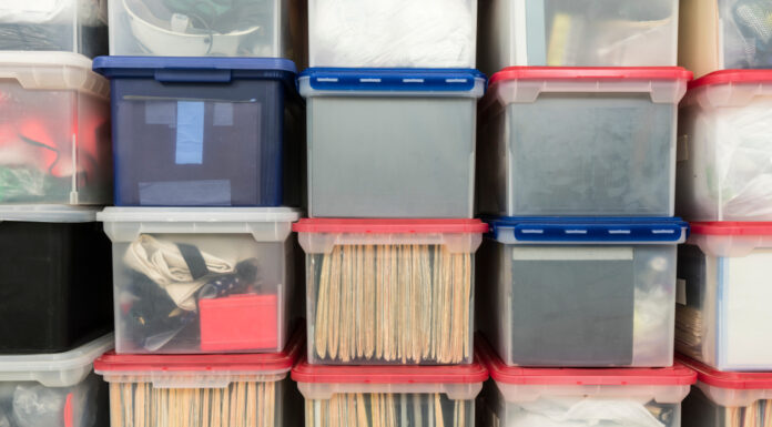 Scatole portadocumenti in plastica impilate con cartelle, raccoglitori e oggetti vari.  