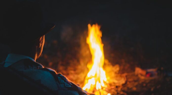 Momento tranquillo e tranquillo nella notte accanto al fuoco, messa a fuoco morbida.  L'uomo con il tradizionale poncho e cappello dei nativi americani si siede accanto al fuoco nel bosco