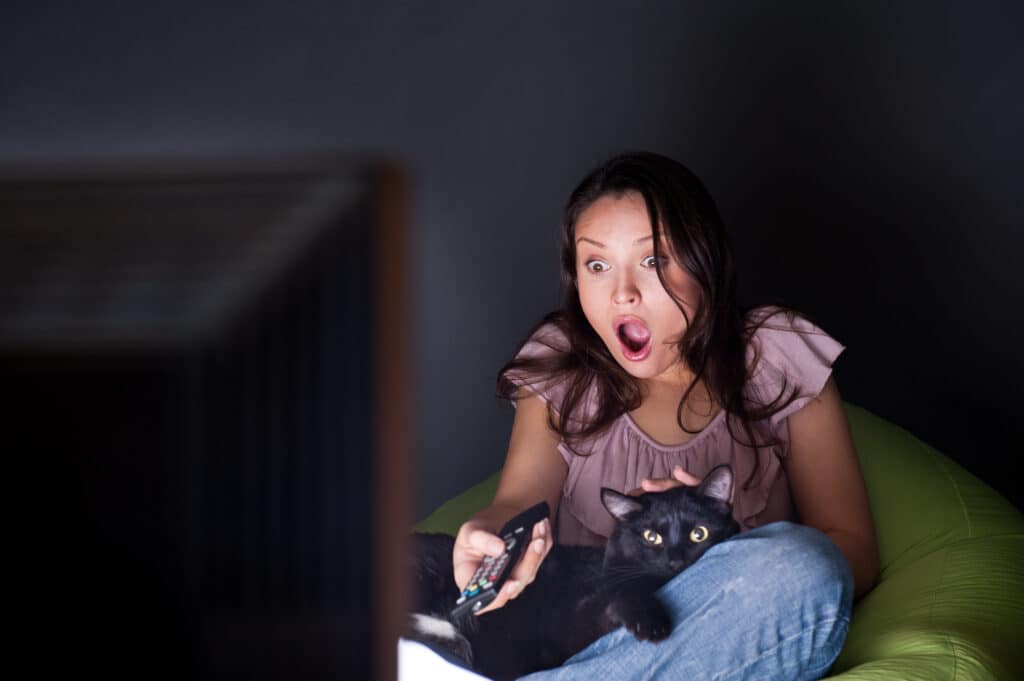 Giovane donna con gatto nero in grembo a guardare la TV al buio