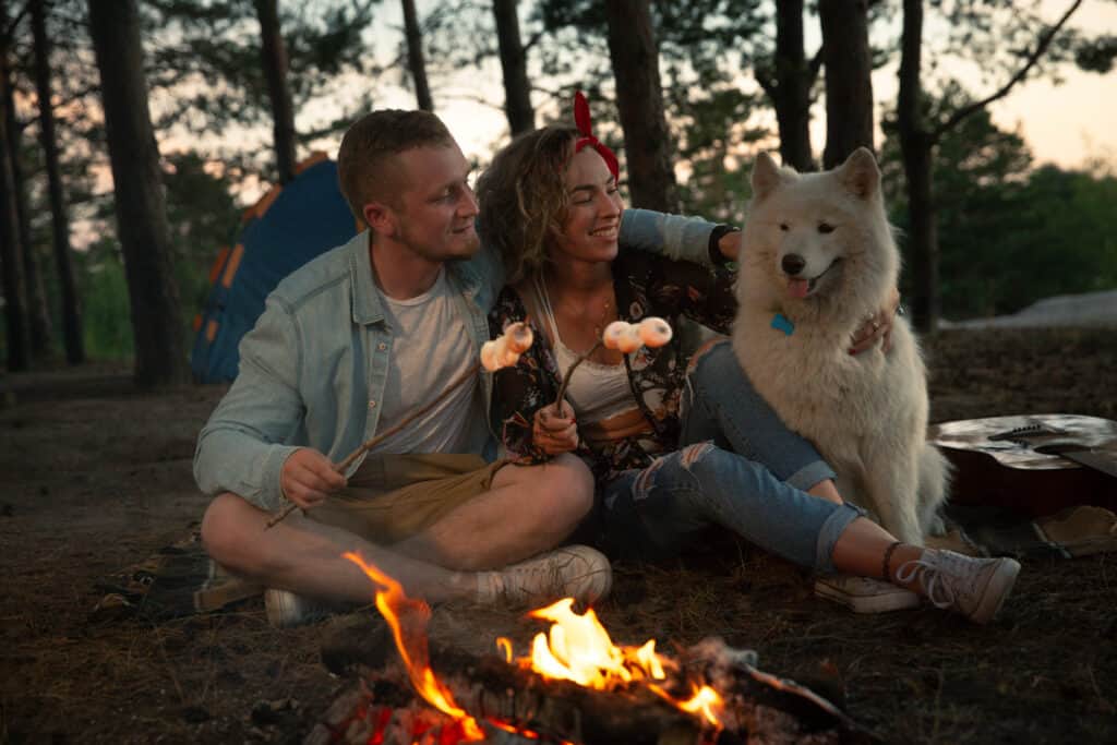 Un ragazzo con una ragazza e un cane accanto al fuoco per brindare ai marshmallow