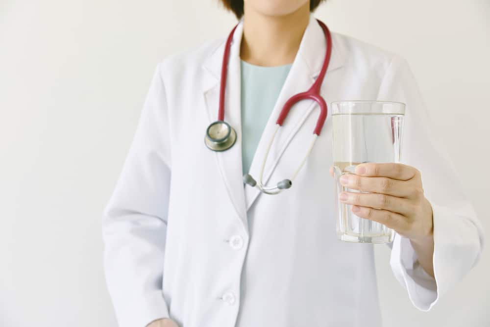 Medico che tiene in mano un bicchiere di acqua fresca e limpida, il medico consiglia di bere acqua sana.