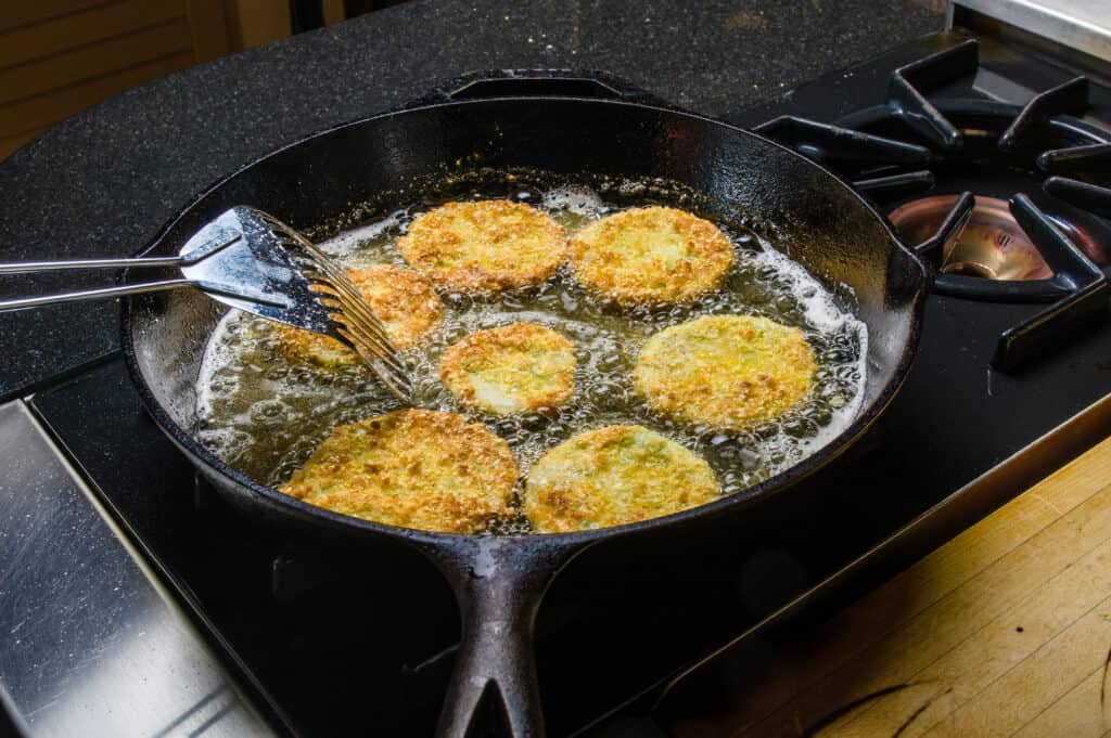 Fette alte di pomodoro verde ricoperte di farina di mais, fritte nell'olio in una padella di ghisa su un fornello a gas. 