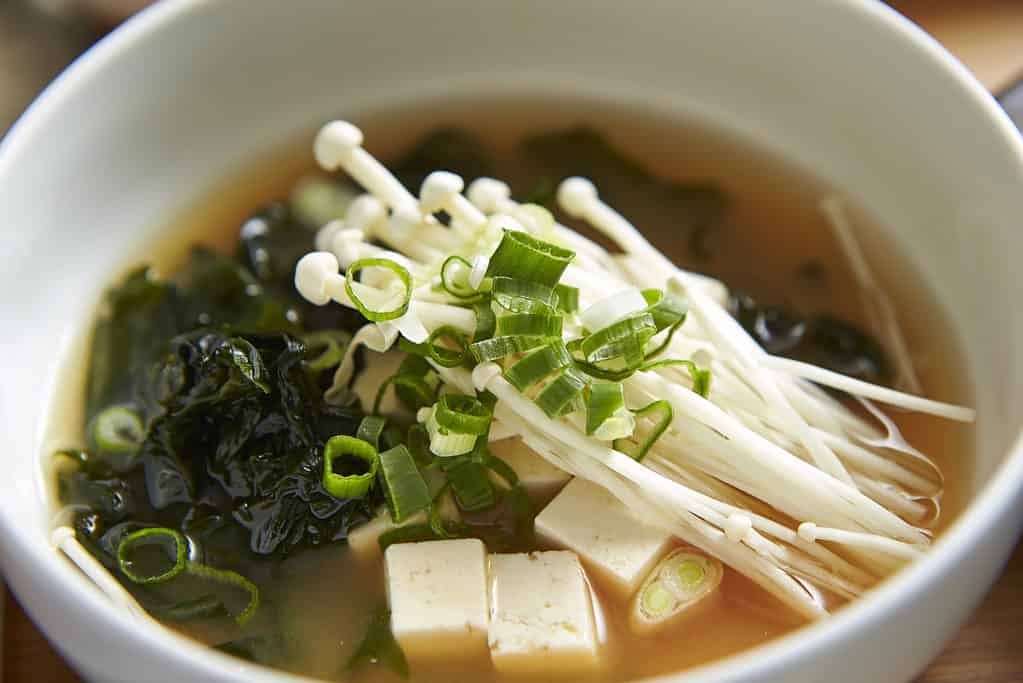 Funghi enoki freschi sopra una scodella di tofu e zuppa di cipolle verdi