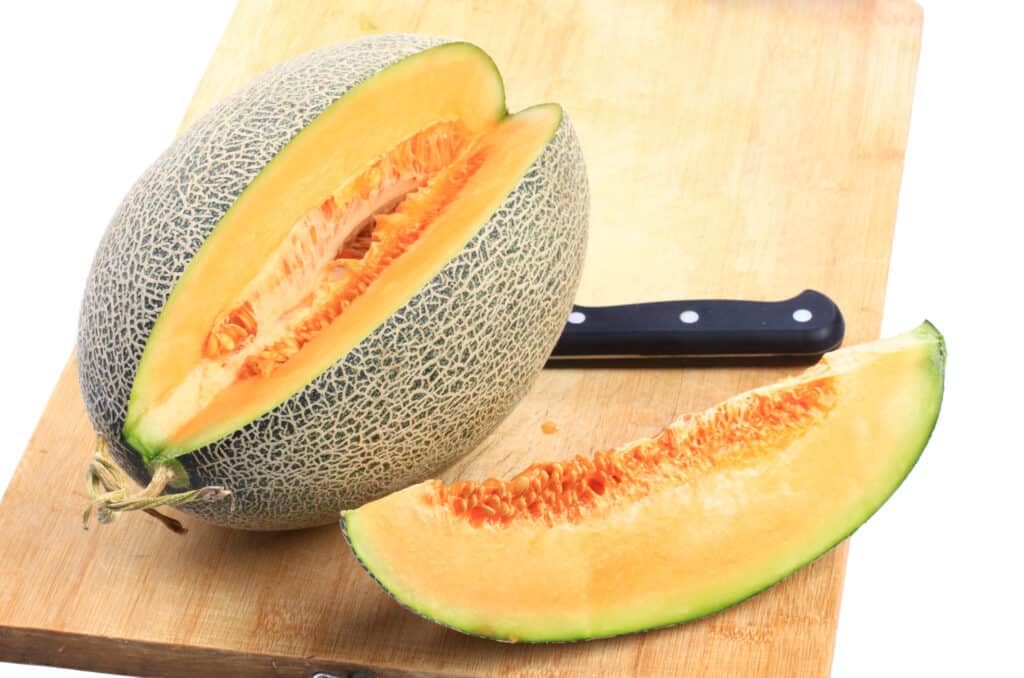 un melone hami (sembra un cantelpe oblungo, anche se la polpa è un po' più chiara) su un tagliere con un cuneo tagliato, un coltello appoggiato sul lato opposto del tagliere. 