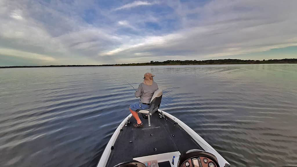 Un uomo si trova su una barca a Milford Lake, pescando con un palo di canna.