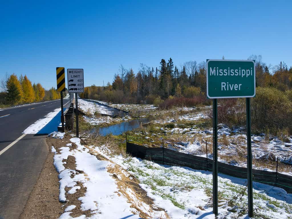 Il fiume Mississippi scorre verso nord vicino alla sua sorgente all'Itasca State Park nel Minnesota.  Questo cartello si trova al quinto ponte autostradale sul fiume Mississippi dopo una nevicata all'inizio dell'autunno.