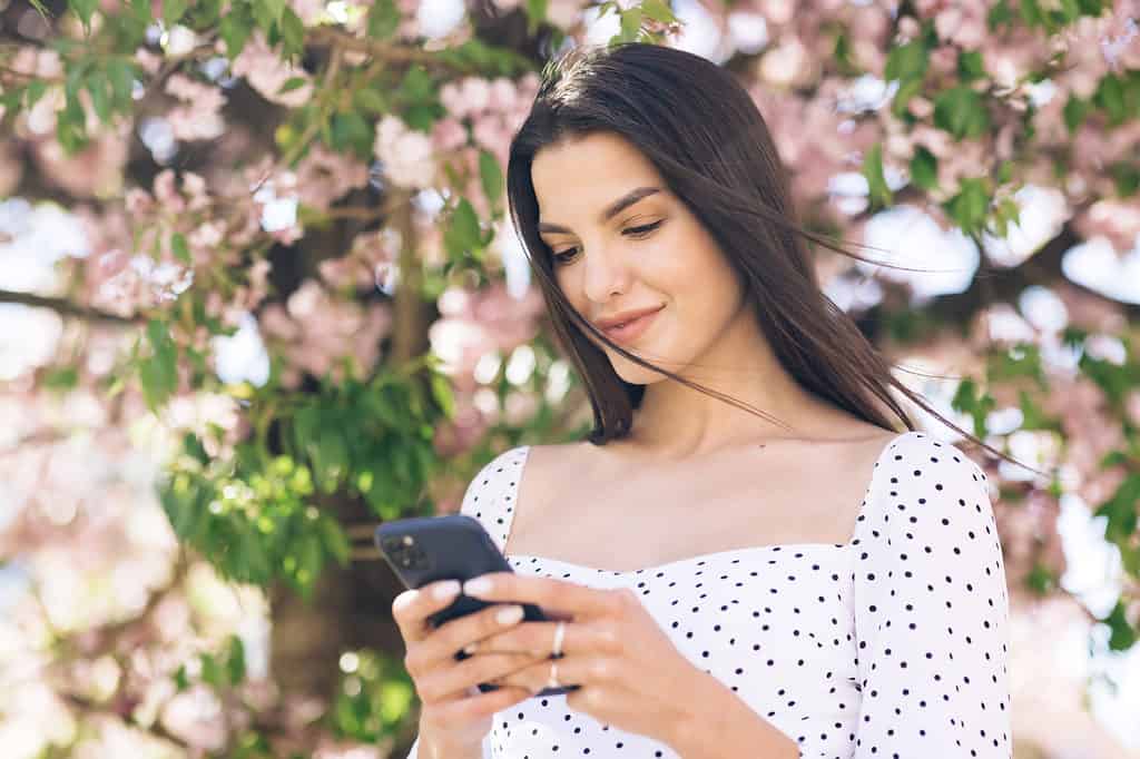 Immagine di una donna che utilizza uno smartphone con fiori di ciliegio sullo sfondo