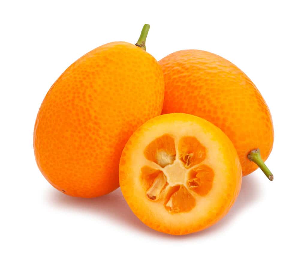 due kumquat interi e uno affettato su uno sfondo bianco