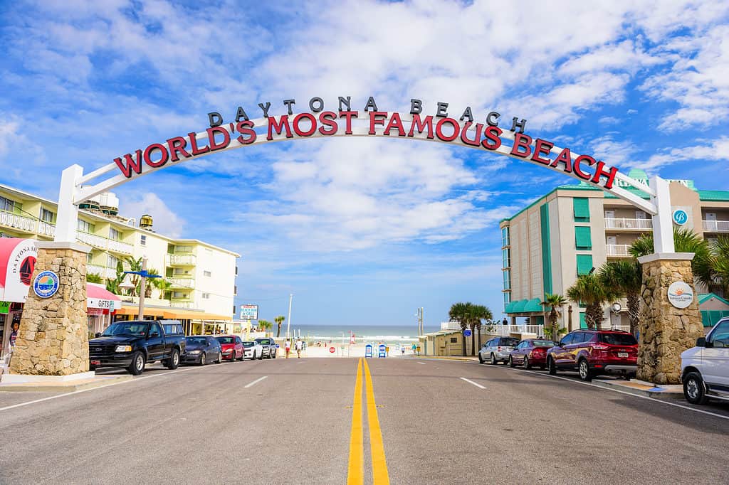 Daytona Beach, FL, USA - 2 febbraio 2015: i bagnanti in lontananza camminano sotto il cartello di benvenuto di Daytona Beach. La popolare destinazione per le vacanze di primavera è soprannominata "La spiaggia più famosa del mondo."