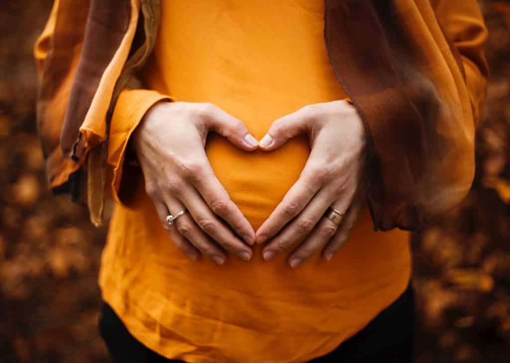 donna incinta che si tiene per mano a forma di cuore sopra la pancia